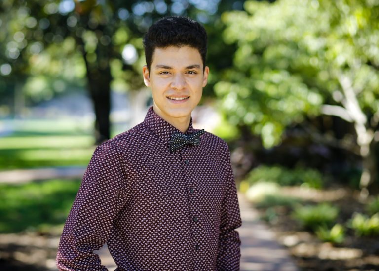 20 year old man with brown hair and brown eyes standing outside under tree with button up shirt and bow tie