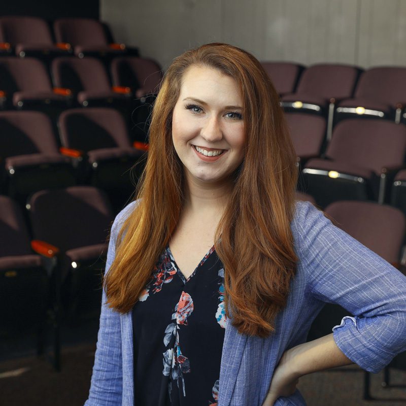 White woman in her early 30s with long auburn hair wearing a light blue blazer