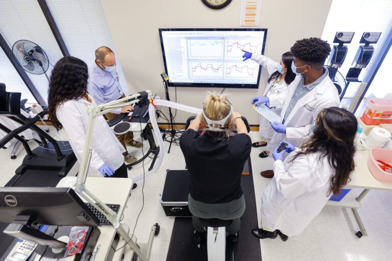 Test subject using stationary bike while Furman students analyze biker's performance.
