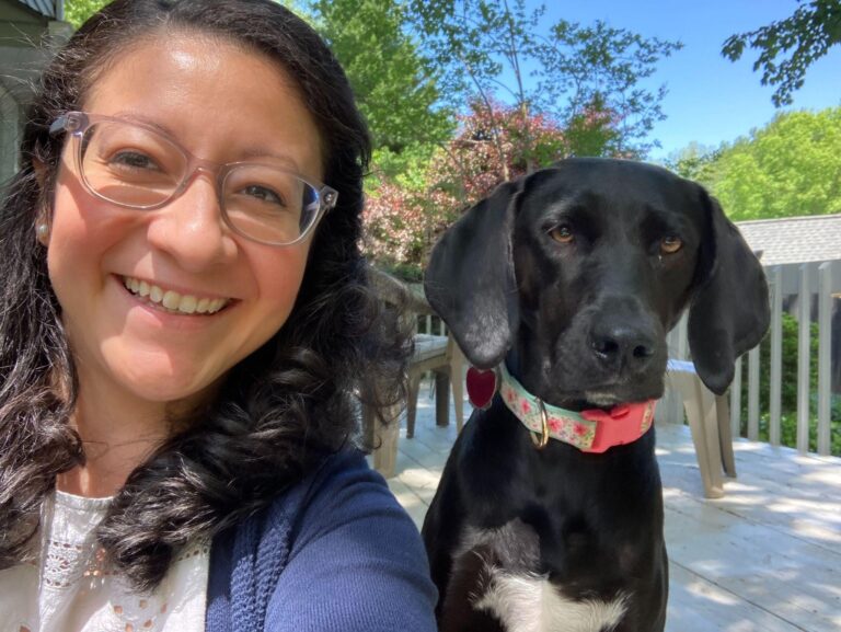 Dr. Veronica Flores. Female with short, brown hair. Posing with her medium sized, short hair dog with a floral colored collar.
