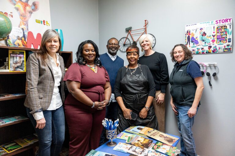 A group of people pose for a photo in a small library they built within a beauty salon to promote literacy and reading among families in the community.