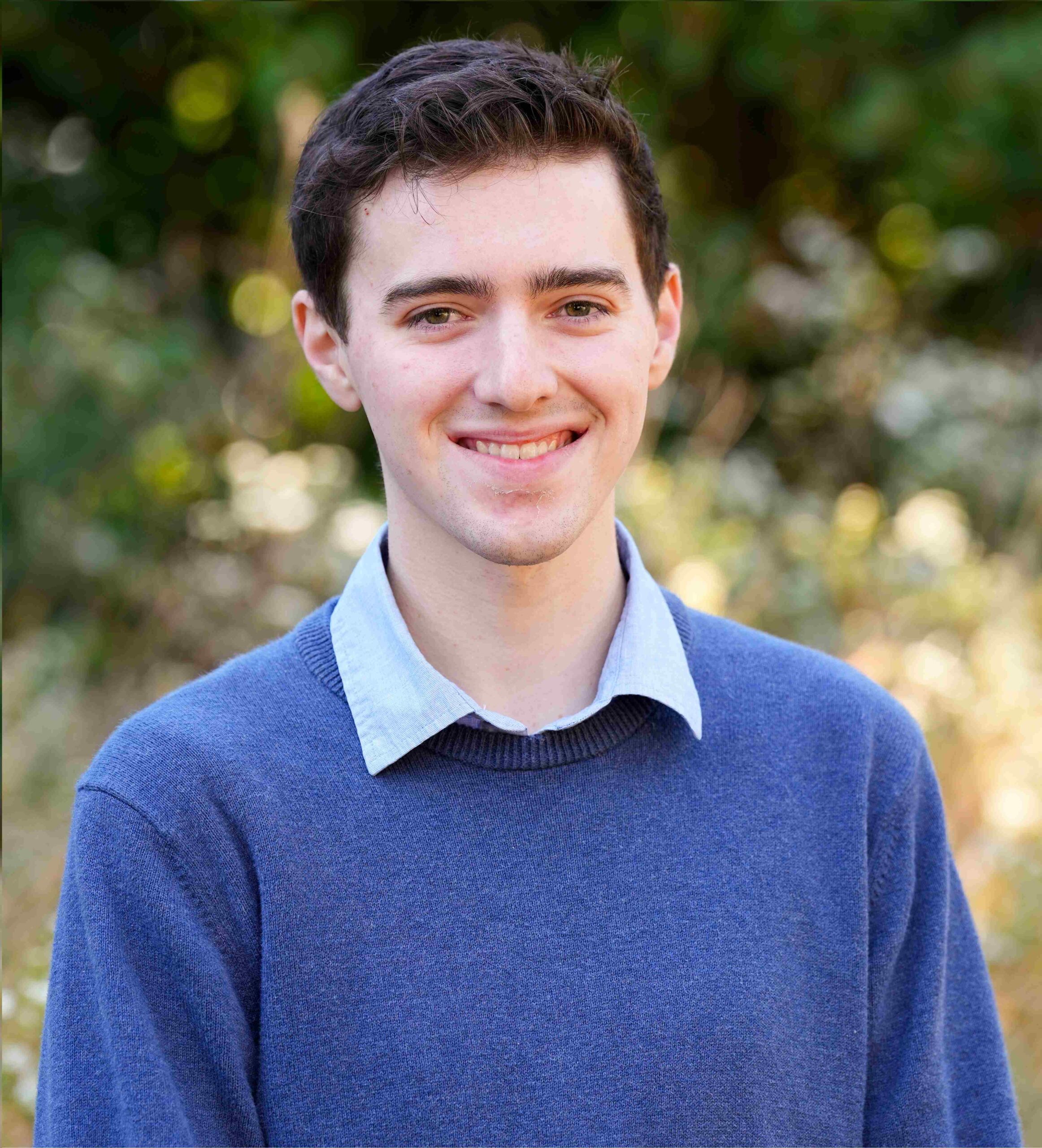 Headshot of Jack Buehner smiling in front of some trees and tall grass between the Furman Farm, Cliffs Cottage, and Greenbelt Community.