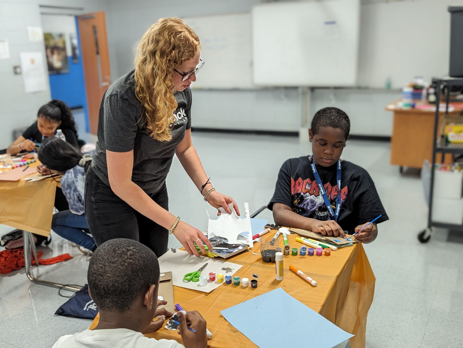 A woman helps young students do a craft in a classroom